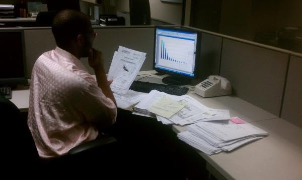 Danny Flight at his old American corporate cubicle before he left the US: grey desk walls, stacks of paperwork, an old monitor and desk phone. The life the geoarbitrage move got him out of.