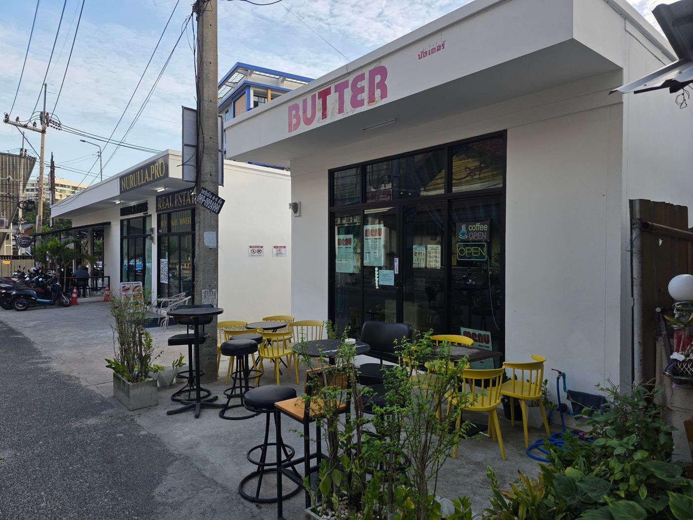 A quiet Pattaya side street with a small minimalist cafe, outdoor seating, and parked motorbikes, photographed by Danny Flight.