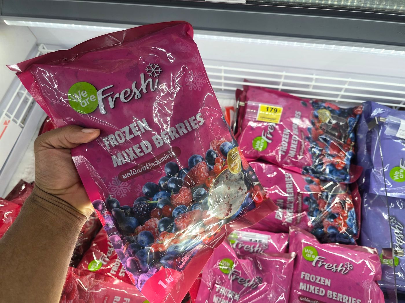A one-kilo bag of frozen mixed berries held up in a Thai supermarket freezer by Danny Flight, with 179 baht tags visible.