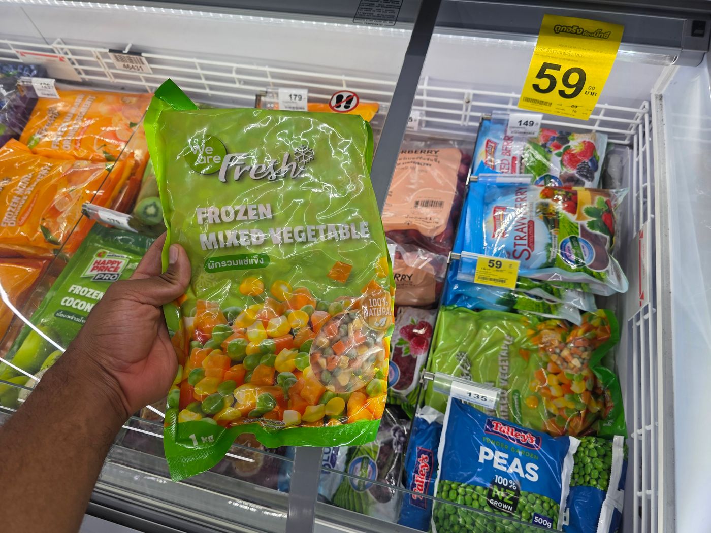 A one-kilo bag of frozen mixed vegetables held up in a Thai supermarket freezer aisle by Danny Flight, with a 59 baht price tag.