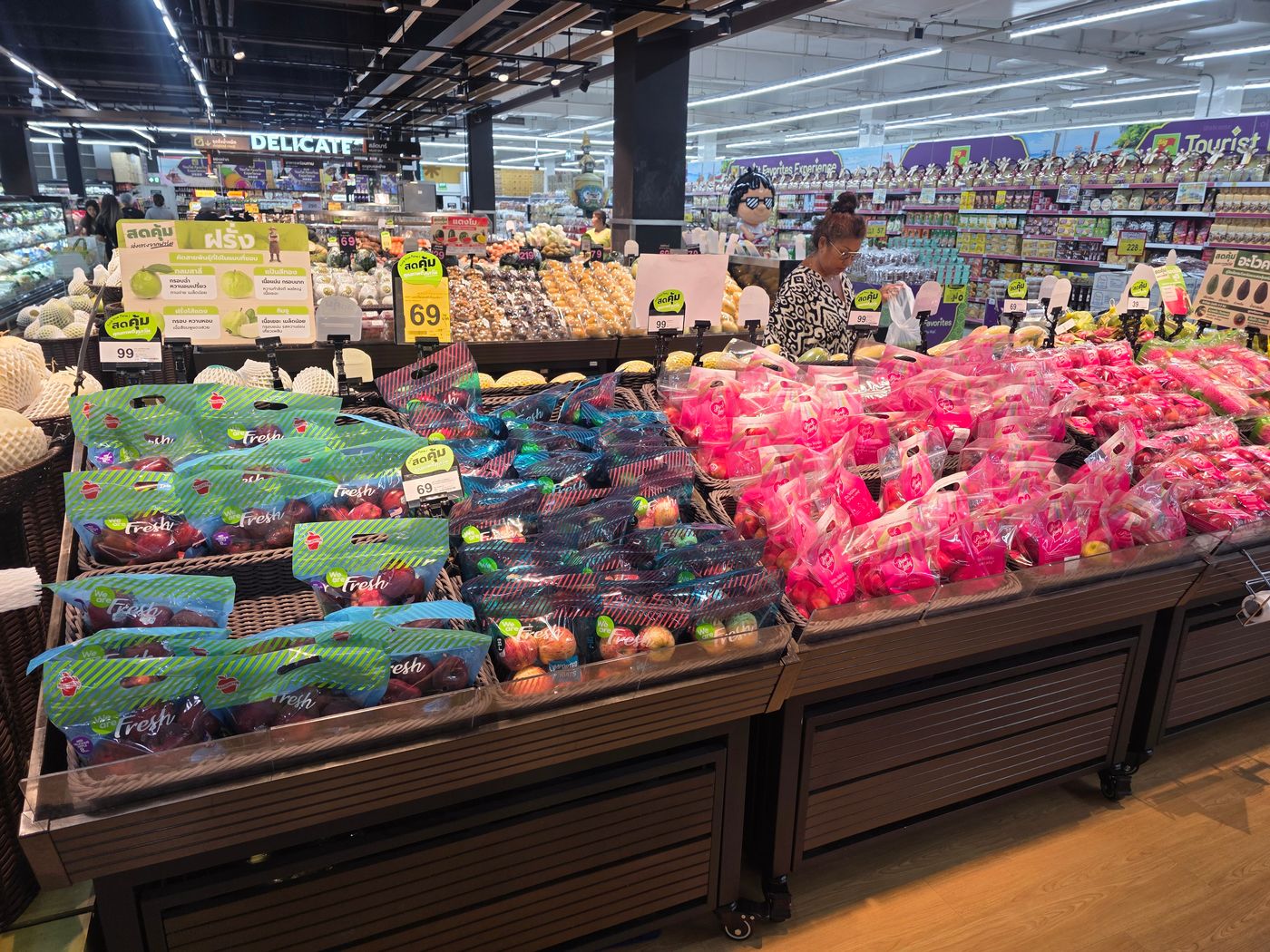 A Thai supermarket produce aisle photographed by Danny Flight with bagged apples, dragon fruit, and guava under 39 to 99 baht price flags.