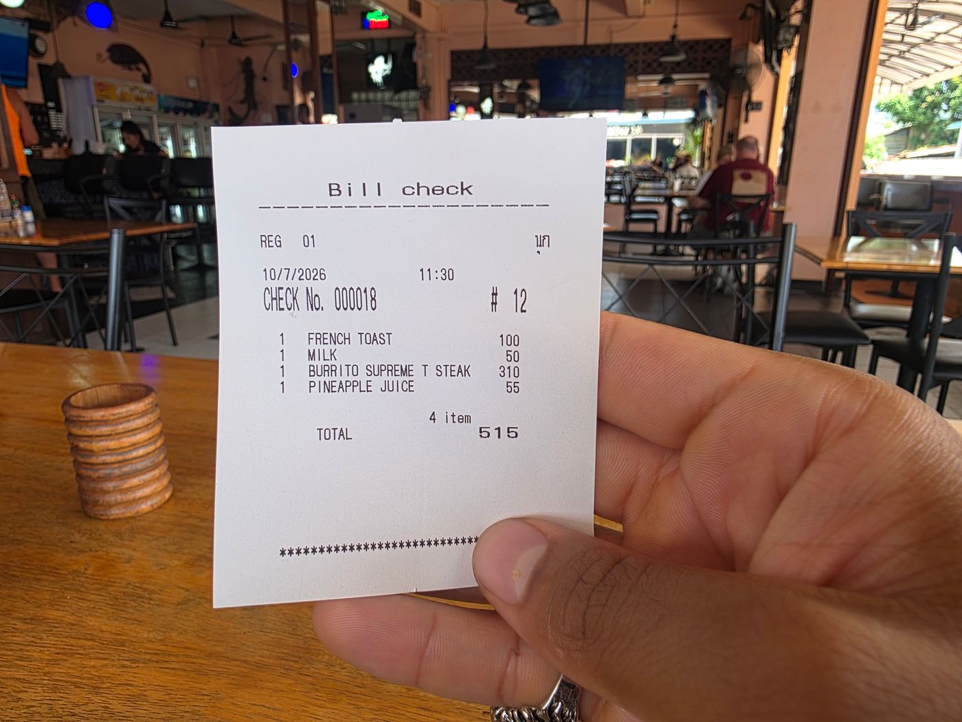 An itemized Pattaya restaurant receipt held by Danny Flight showing French toast 100 baht, milk 50, burrito supreme steak 310, pineapple juice 55, total 515 baht.
